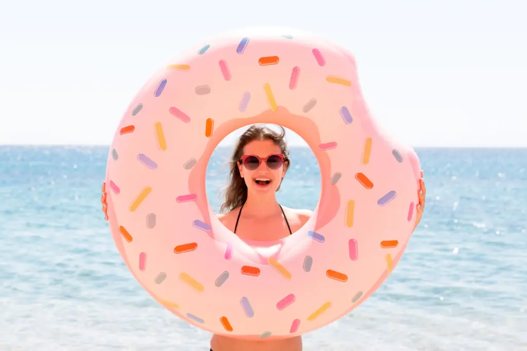 Chica sonriendo en la playa con un flotador en forma de donut