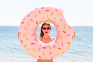 Chica sonriendo en la playa con un flotador en forma de donut