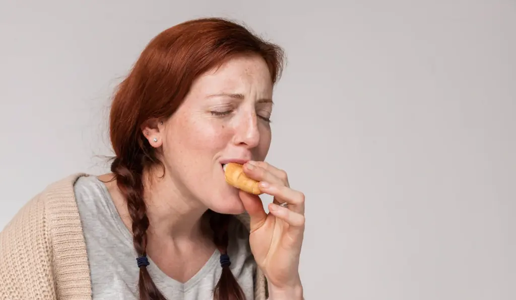 Mujer comiendo un croissant por el lado izquierdo de su boca